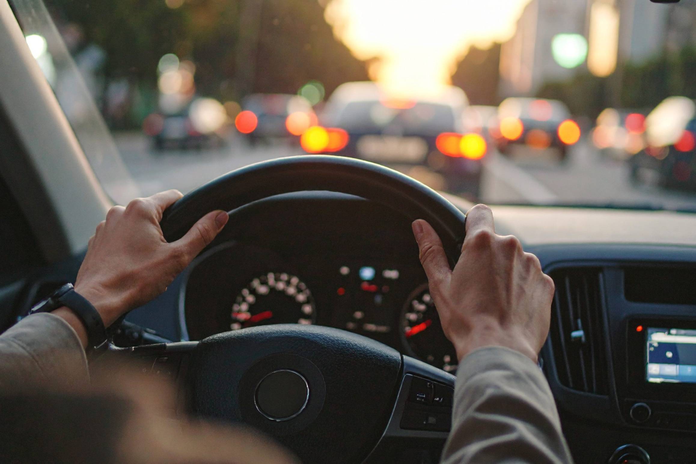 Mani sul volante di un'auto nel traffico cittadino al tramonto