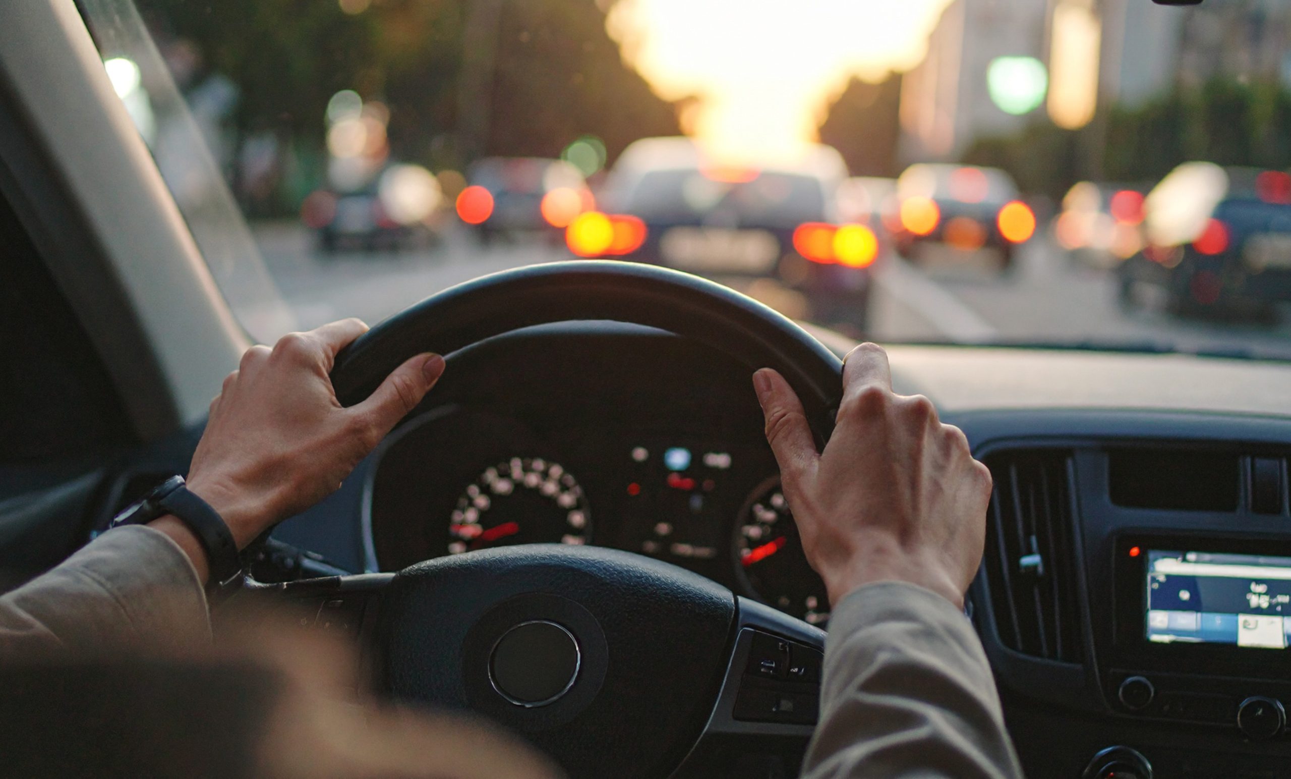 Mani sul volante di un'auto nel traffico cittadino al tramonto
